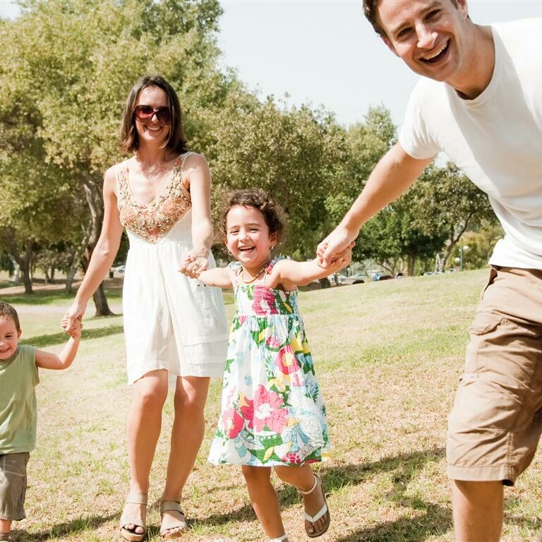 Young family playing and running with two young children, focus on the father