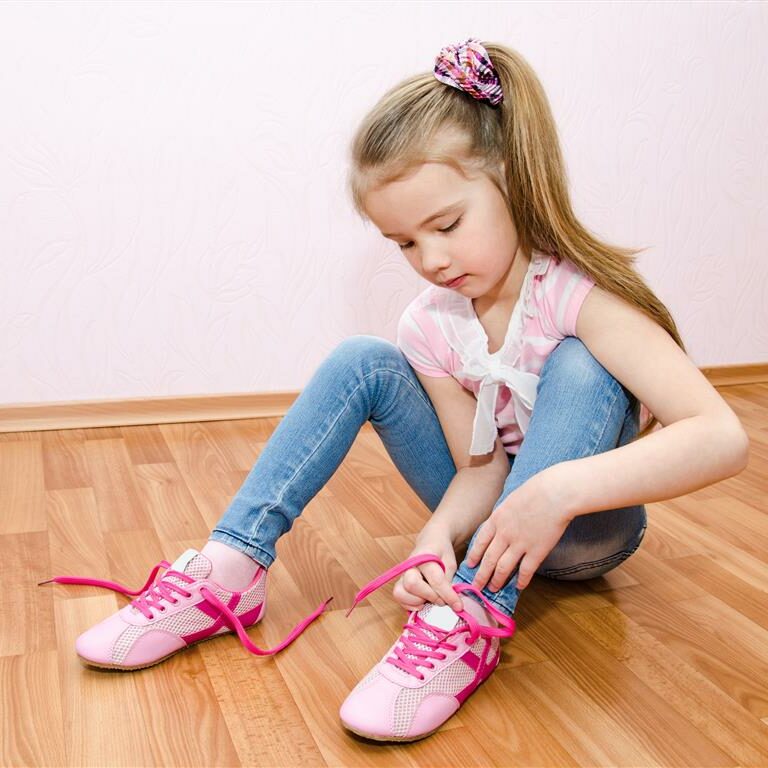 Cute smiling little girl tying her shoes at home